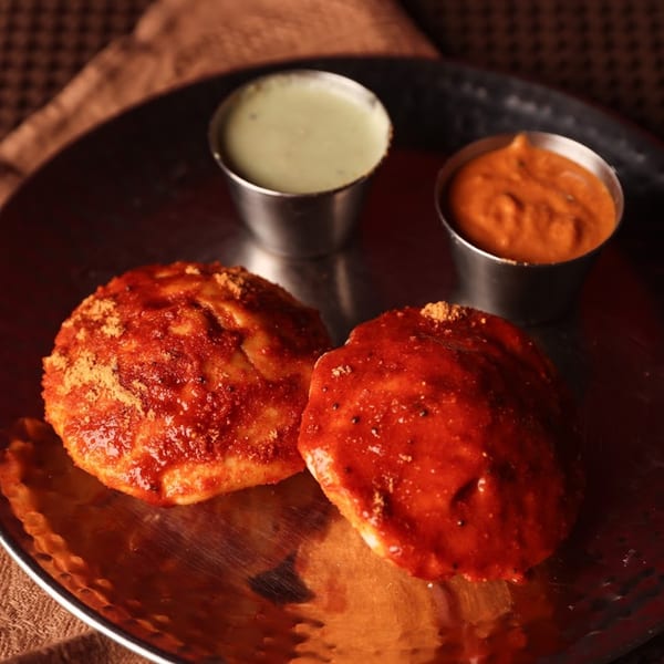 Two red masala idlis with green and orange chutneys on a silver plate at Chaska Indian Restaurant.