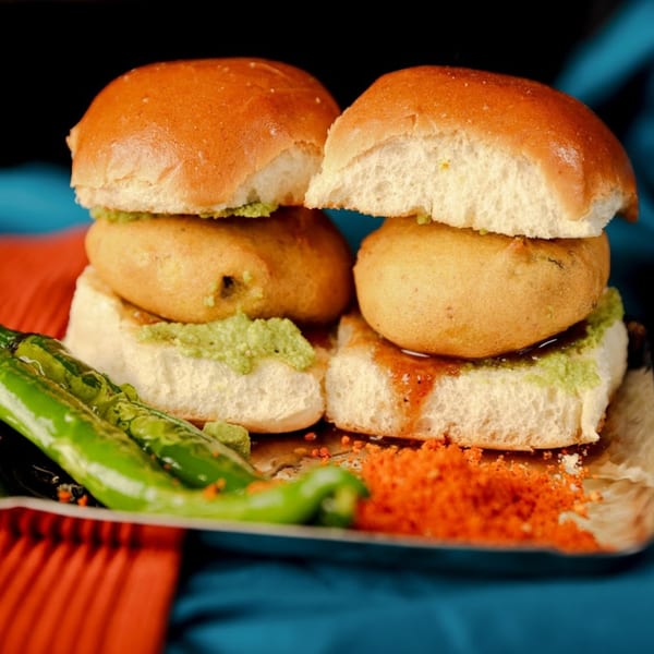 Two Indian vada pavs with green chutney, red spice powder, and green chilies.