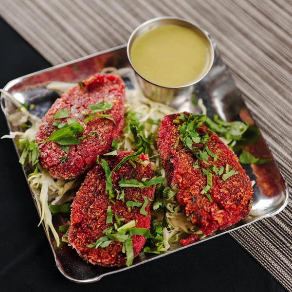 Three vibrant red Indian cutlets, garnished with cilantro, served on shredded cabbage with a side of green chutney.