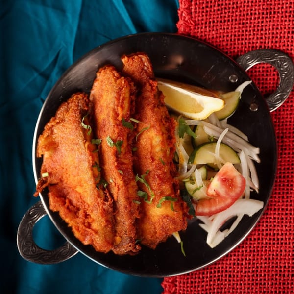 Chaska Indian Restaurant's fried fish with lemon, onions, cucumbers, and tomatoes in a black bowl.