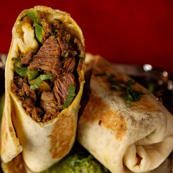 Two Chaska Indian Restaurant burritos, one open revealing spiced meat and green peppers, on a red background.