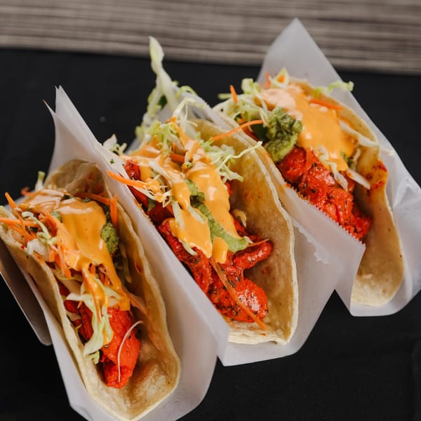 Three Indian-style tacos with red chicken, shredded cabbage, carrots, and two sauces.